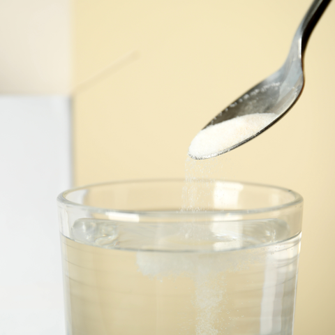 Spoon holding vitamin C powder above a glass of water
