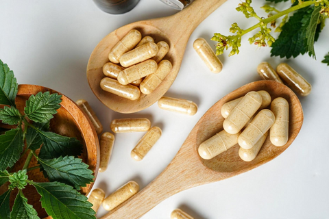 Mortar and pestle with a wooden spoon full of pills on a light wooden surface.