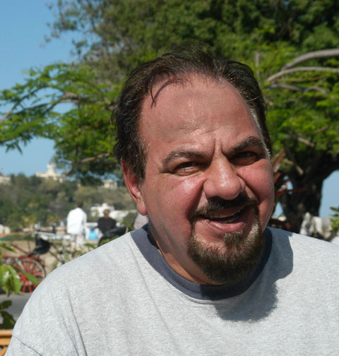Man named Bill Coury with a beard and mustache wearing a gray shirt outdoors with trees and people in the background