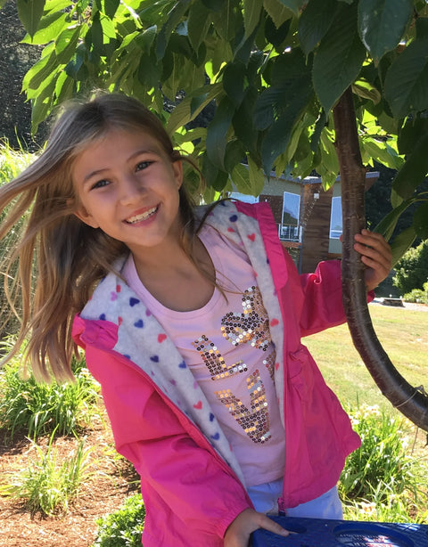 Young girl in a pink jacket standing outdoors near a tree