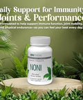 A white bottle of Noni dietary supplement by American Nutriceuticals, displayed on a wooden slice pedestal surrounded by green foliage. The background is a soft olive green with promotional text at the top reading 'Daily Support for Immunity, Joints & Performance'.